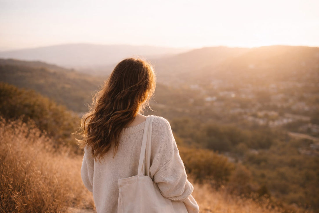 A woman standing on a sunlit hillside, looking toward the horizon, representing quiet courage, self-trust, and new beginnings.