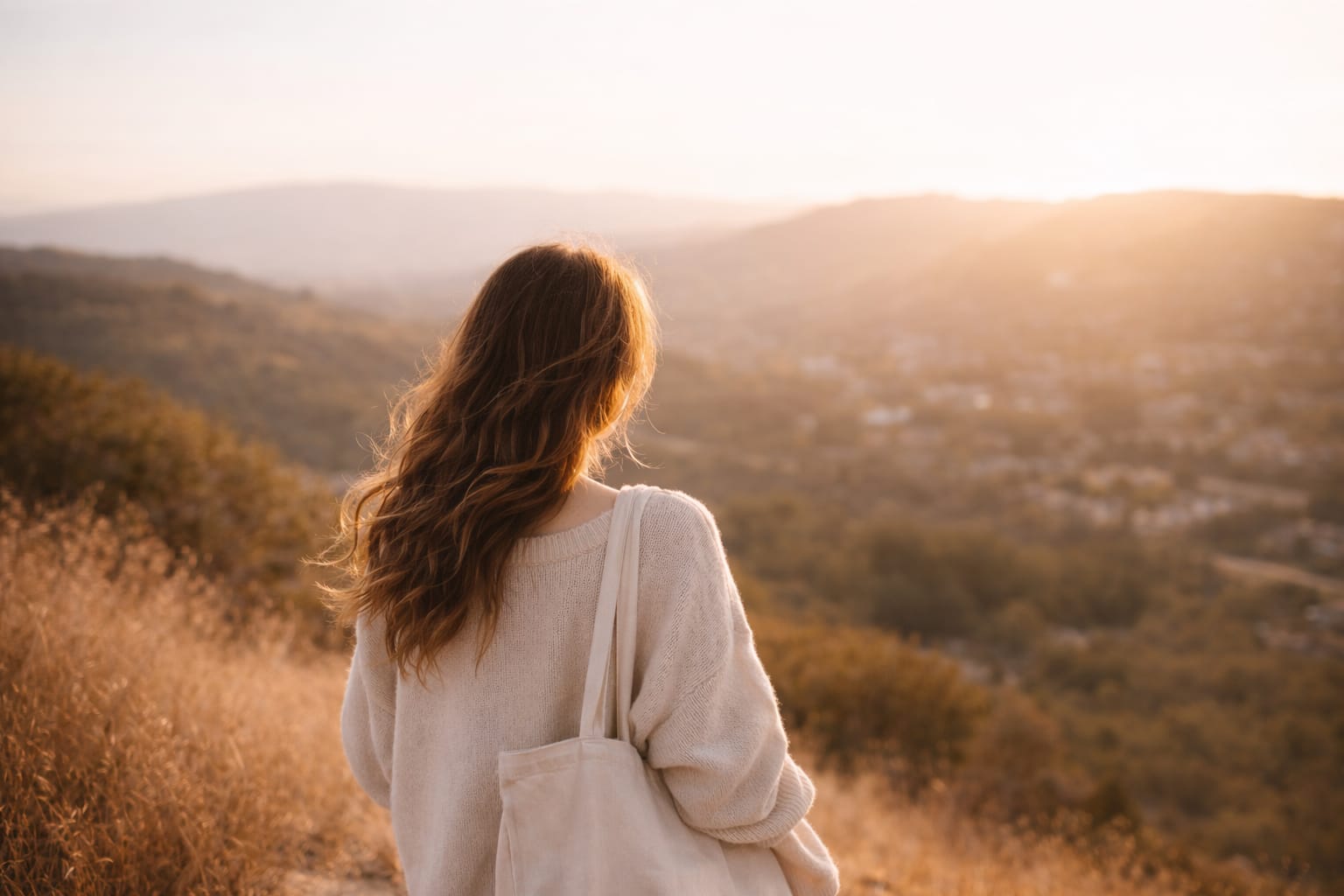A woman standing on a sunlit hillside, looking toward the horizon, representing quiet courage, self-trust, and new beginnings.